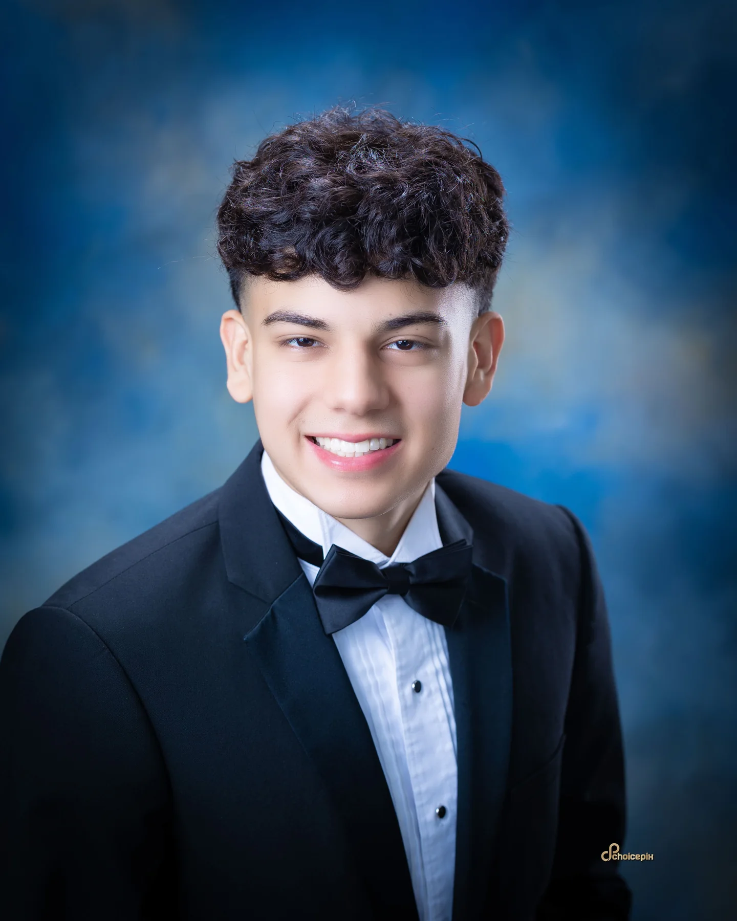 Senior portrait in a tuxedo against a painted blue backdrop
